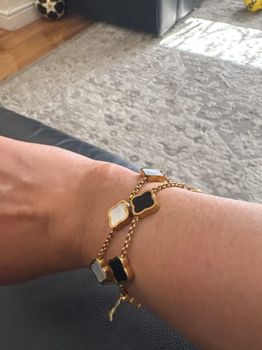 Customer wearing two layered Celine Clover Bracelets on their wrist, one with black and one with white motifs.