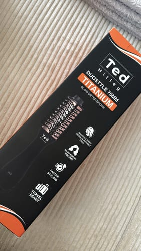 Recensent toont de verpakking van de Ted Hilley DuoStyle Titanium fohnborstel op een getextureerde ondergrond.