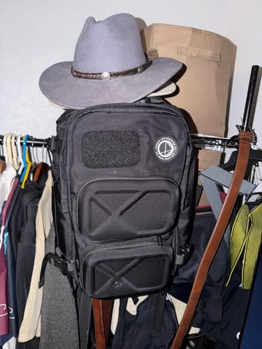 Reviewer's black Ocean Tactical Backpack hanging on a clothing rack with a hat on top.