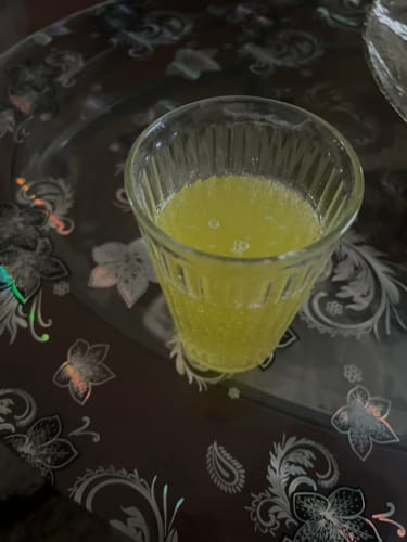 Customer's prepared collagen supplement, a yellow bubbly drink in a glass, on a patterned table.