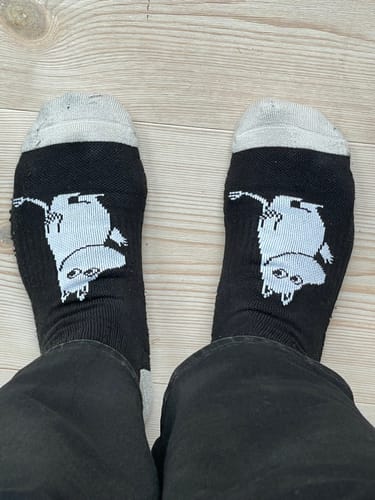 Anmelders sorte Moomin ankelstøttestrømper vist på fødderne på et trægulv.