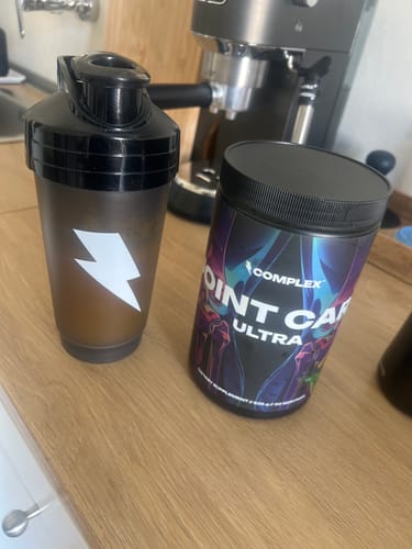 Customer's tub of Joint Care Ultra on a wooden counter next to a black shaker bottle.