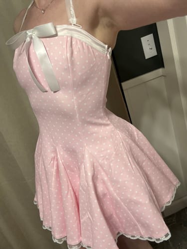 Close-up of a reviewer wearing the pink Dolly Polka Dot Dress with its white bow and halter straps.
