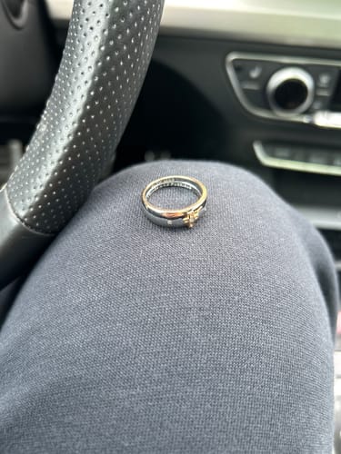 Customer's two-tone gold cross ring resting on their leg in a car.