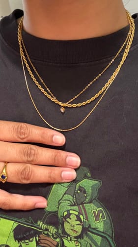 Close-up of a customer wearing the gold twisted chain necklace layered with two other necklaces against a black t-shirt.