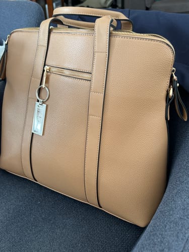 A customer's latte Rhodes Laptop Bag, showing its size and pebbled texture while resting on a blue armchair.