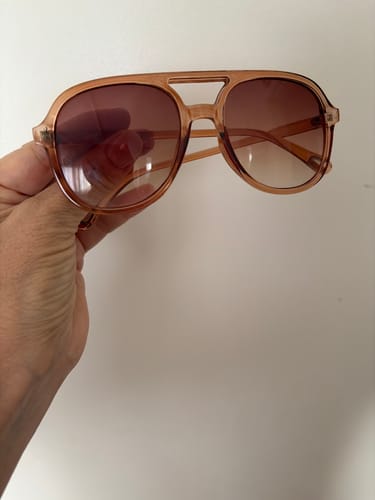 Cliente segurando os óculos Levone, que possuem uma armação translúcida e lentes em degradê marrom.
