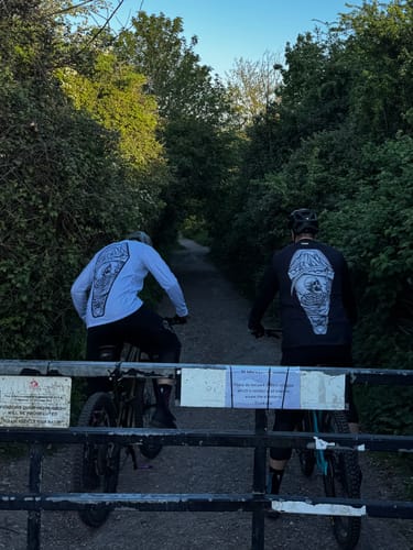 Two customers on mountain bikes seen from behind wearing black Cryptkeeper All Season Trail Shorts on a wooded trail.