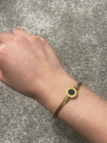 Reviewer's wrist wearing the Melinda Gold Bangle, with the round, black side of the reversible charm showing.