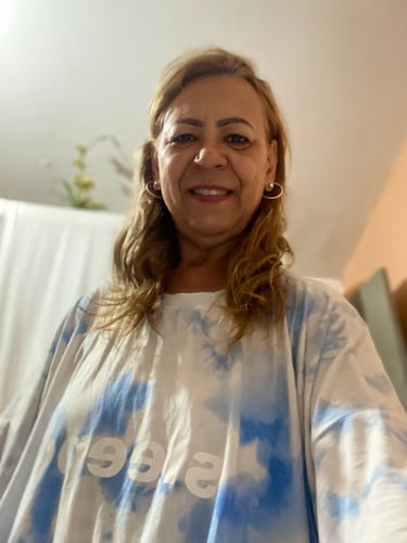 Consumidora sorrindo em uma selfie usando a Camisola Tie Dye, que tem um padrão azul e branco.