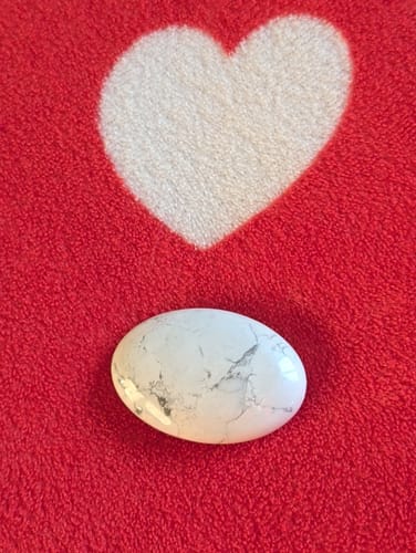 Cliente montrant son galet d'Howlite sur un tissu rouge avec un cœur blanc.