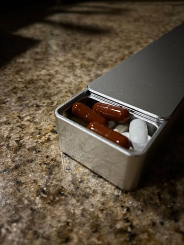 Close-up of a customer's open metal Weekly Case on a counter, filled with various vitamin pills.
