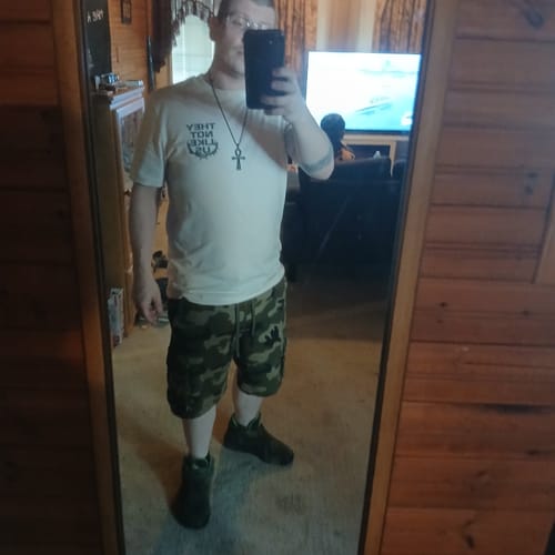 Customer taking a mirror selfie while wearing the light-colored NOT LIKE US TEE with camo shorts.