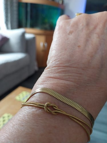Reviewer's wrist with the gold Forever Knot Bracelet worn next to another flat chain bracelet.