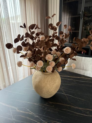 Recensent toont de beige Arda vaas, gevuld met een groot boeket, op een donkere tafel.