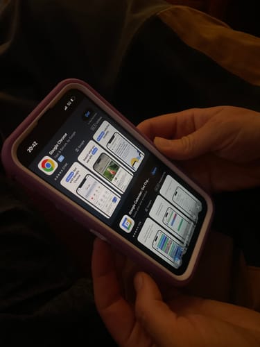 Customer holding their Apple iPhone 14 Pro in a purple case, with the App Store visible on the active screen.