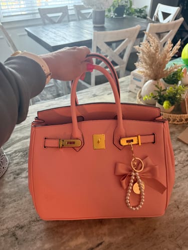 Customer holding their pink structured Warkin Bag open on a counter, showing its gold hardware and a charm.