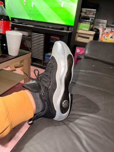 Reviewer showing the side profile of the black AG 6 "AG Ion" shoe with its wavy sole.