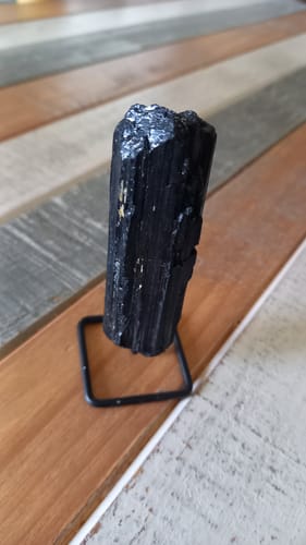 Un client montre sa petite tourmaline noire sur son socle, posée sur une table en bois.