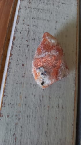 Photo d'un client : gros plan sur la pierre de soleil brute orange et blanche sur une surface en bois.
