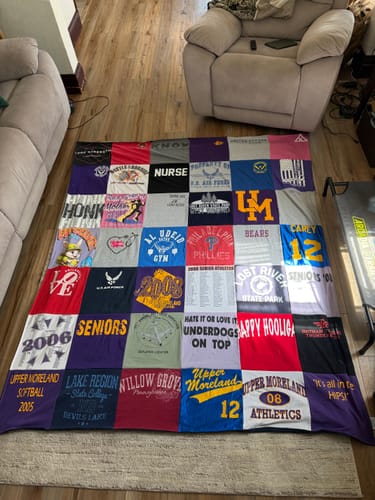 Customer's colorful Project Repat T-Shirt Quilt spread out on a living room floor, showing various t-shirt designs.