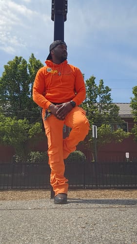 Customer poses outdoors in a bright orange 'Drip Harder' hoodie and matching stacked pants.