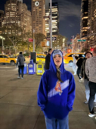 Reviewer wearing the surf's up blue hoodie with the hood up on a city street at night.