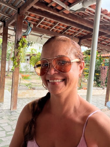 Avaliadora sorrindo em uma selfie, usando os Óculos Savona com armação dourada e lentes laranja.