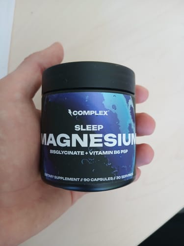 Customer holding the black jar of Sleep Magnesium supplements in their hand against a light wooden surface.