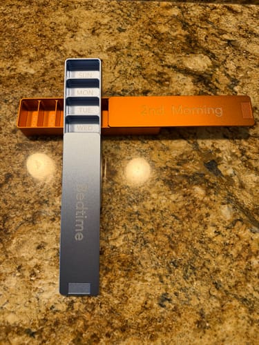 Reviewer's orange and silver metal pill cases on a counter. The silver "Bedtime" case is open, showing daily compartments.