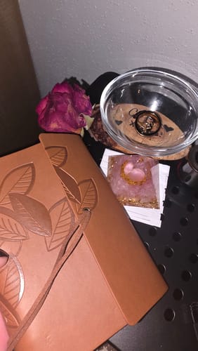 Customer displays items from their AuraBloom Subscription Box, including a brown journal, a crystal, and a dried flower.