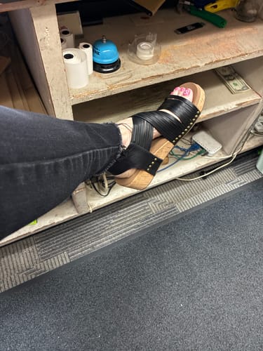 Customer showing a side view of the black wedges on their foot, paired with black jeans.