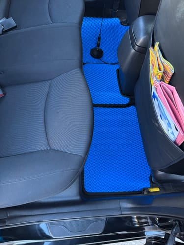 Recenzent pokazuje niebieskie, dopasowane dywaniki samochodowe na podłodze tylnych siedzeń.