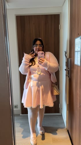 Reviewer taking a mirror selfie in the pink Dolly Polka Dot Dress, styled with a matching cardigan and tights.