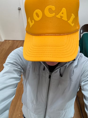 Reviewer wearing the yellow Tonal Local Trucker hat, shown from a top-down perspective indoors.