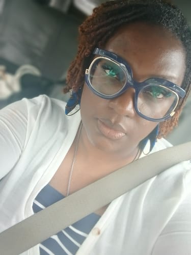 Close-up of a reviewer wearing the Blue Bowtie Hoop Earrings, which are partially visible behind large glasses.