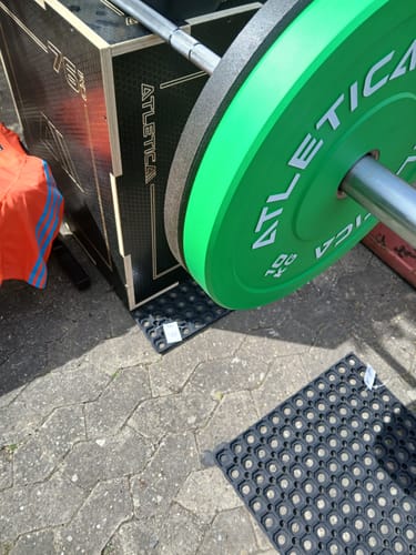 Eine grüne Color Bumper Plate des Rezensenten auf einer Hantelstange vor einer Box in einem Outdoor-Gym.