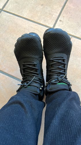 Ein Kunde zeigt die getragenen schwarzen Vitality V - Barfußschuhe aus der Vogelperspektive.