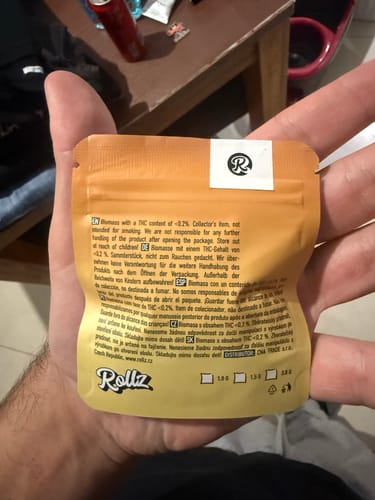 Reviewer's hand holding the back of the yellow pouch for California Love THCA Flower.