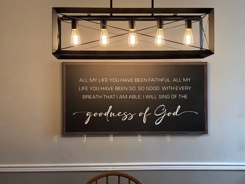 Customer's Goodness Of God Faith Sign II hanging on a dining room wall below a modern light fixture.