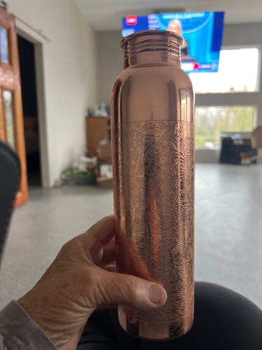 Customer holding a tall copper water container with a decorative hammered design.