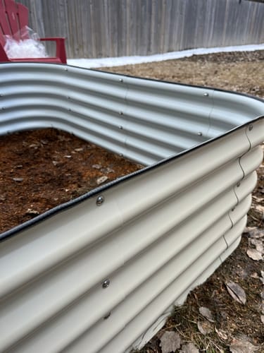 Close-up of a reviewer's off-white modular garden bed, showing the corrugated steel corner and soil inside.