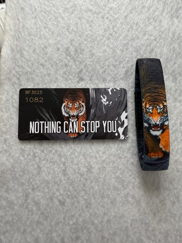 Reviewer's 'Nothing Can Stop You Tiger Bracelet' and collector's card with a bold tiger graphic, laid on a gray surface.