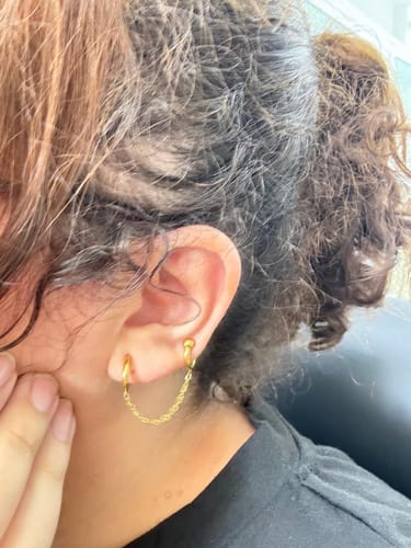 Cliente con el Ear Cuff con extensión dorado puesto en la oreja, con dos aros unidos por una cadena.