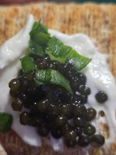 Customer's close-up of black caviar with chives and cream, served on a piece of toast.