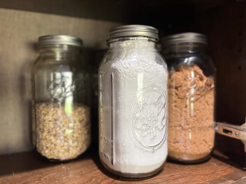 Reviewer's pantry shelf with three mason jars of dry goods sealed by the Mason Genie.