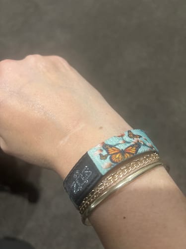 Customer's wrist wearing the colorful Butterfly Kisses Bracelet, stacked with two gold bracelets.