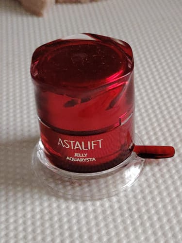 Customer's red jar of Astalift Jelly Aquarysta shown in its clear holder on a textured surface.