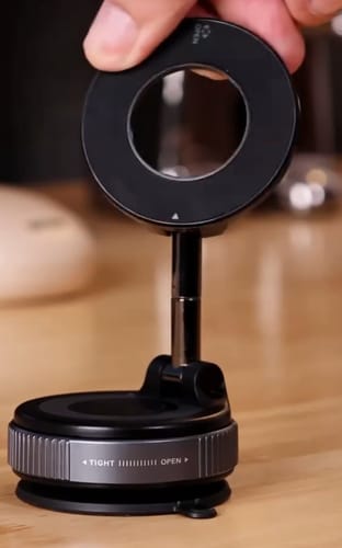 Customer holding a black, ring-shaped device mount with a twisting suction base on a wooden desk.