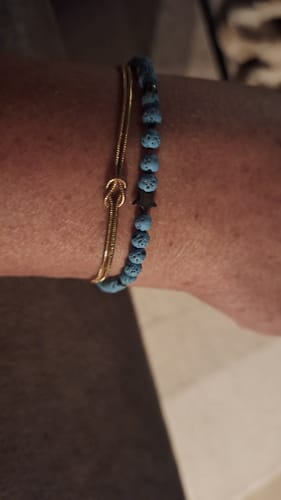Close-up of a reviewer wearing the gold-colored Forever Knot Bracelet on their wrist next to a beaded bracelet.